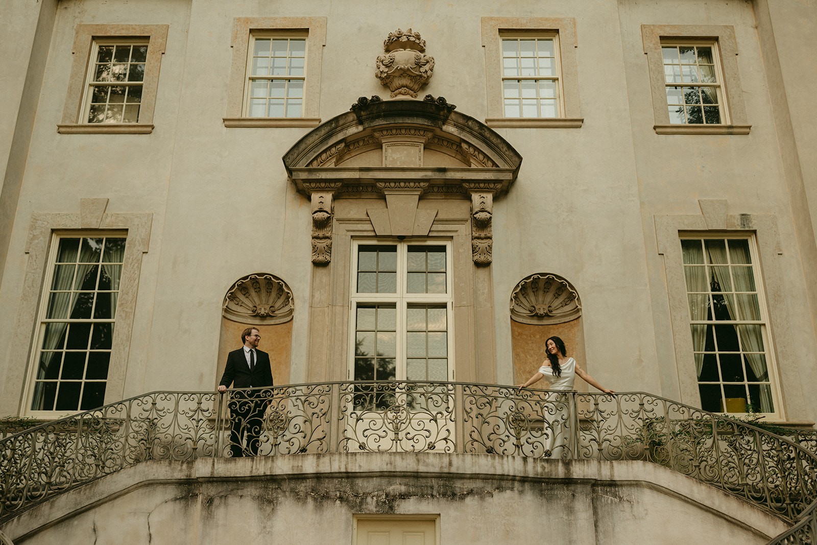 Rachel and Jack at either end of a curved iron balcony, smiling at each other