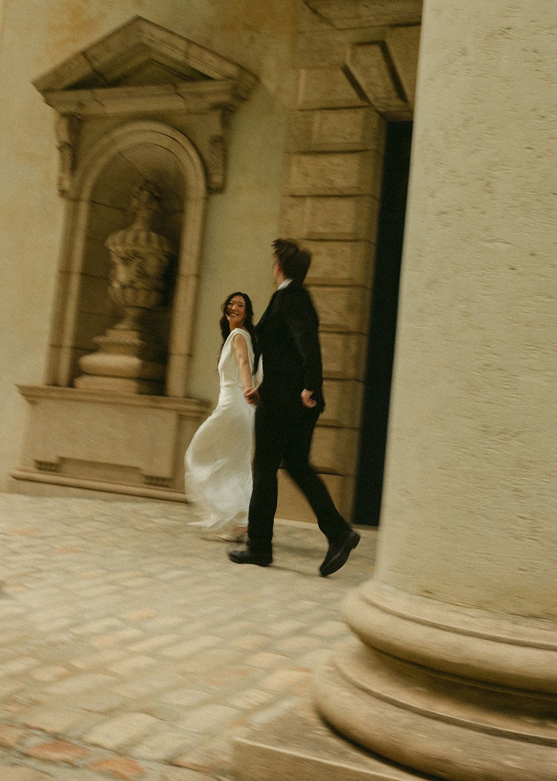 Rachel looking back over her shoulder as she and Jack walk through a stone courtyard