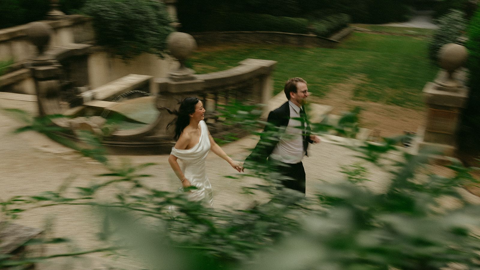 Rachel and Jack running hand in hand past a stone fountain